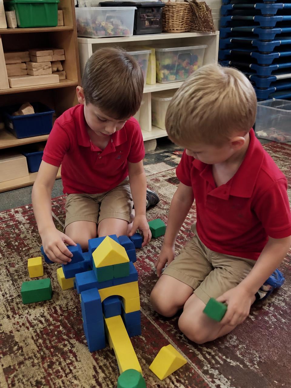 Illustration of two preschool boys in red KCA polos building with foam blocks on a classroom rug