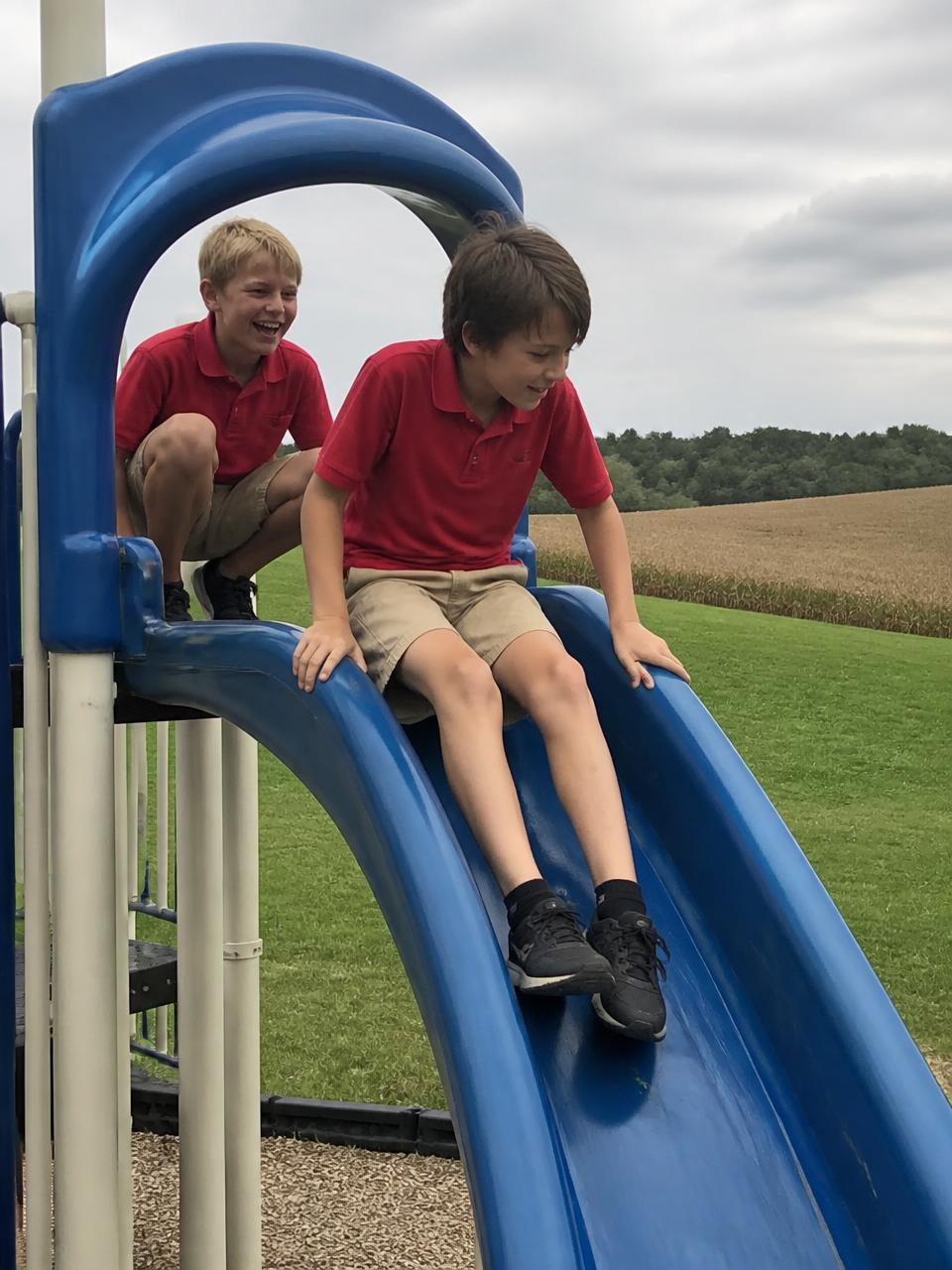 Illustration of two young students in red polos at the top of the blue playground slide